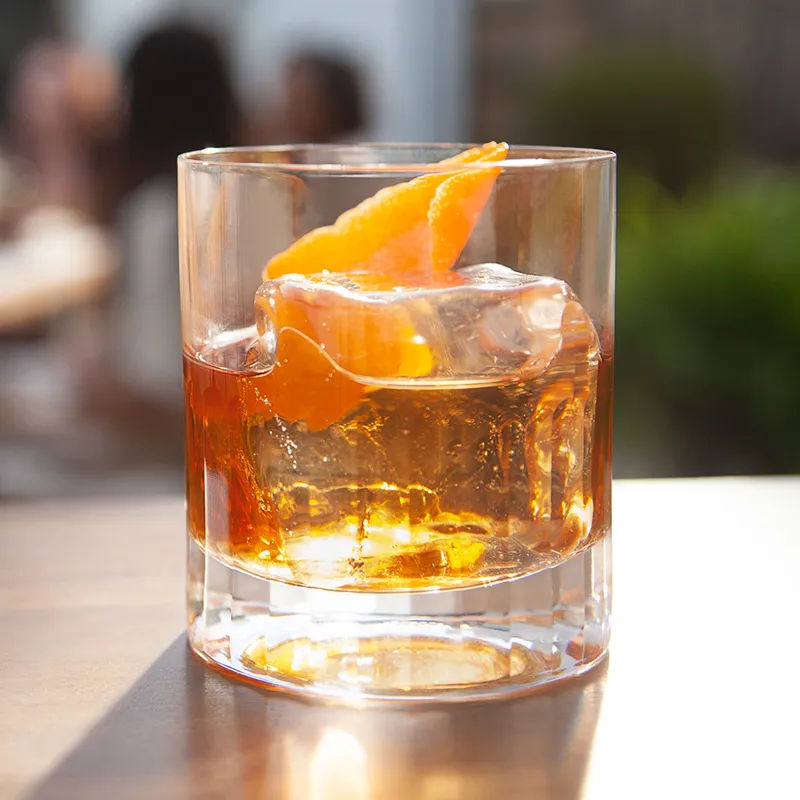 A glass of summer manhattan garnish with ice cube and orange peel